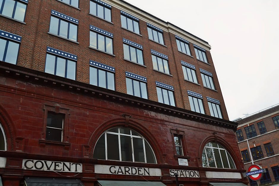 A multi-storey brick building with a ground floor featuring arched windows and the sign ‘COVENT GARDEN STATION’ in black lettering on a white background. Above the entrance, several rows of rectan